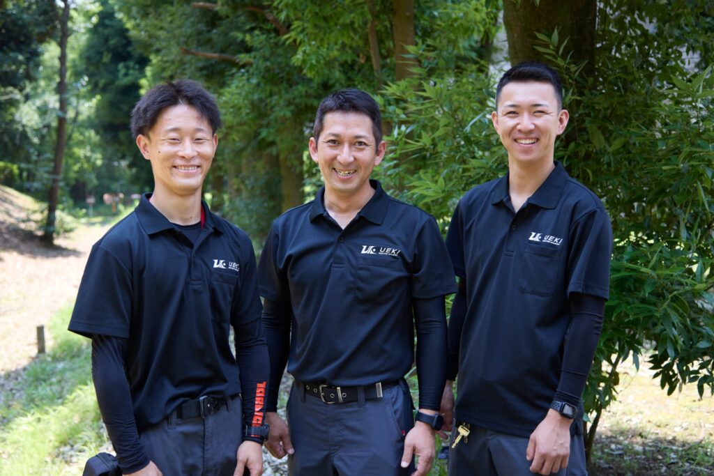 屋外で並んで笑顔を見せる代表取締役 植木紀雄と2人のスタッフ